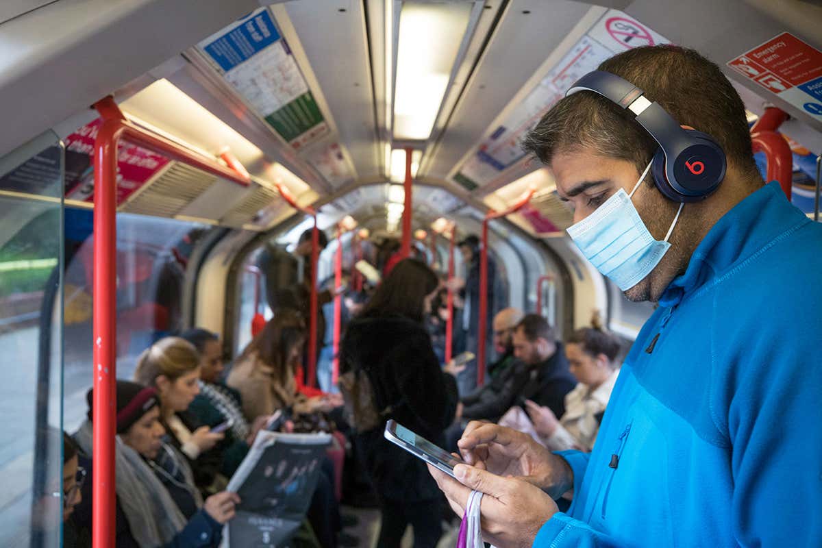 Man on train wearing mask and looking at his phone