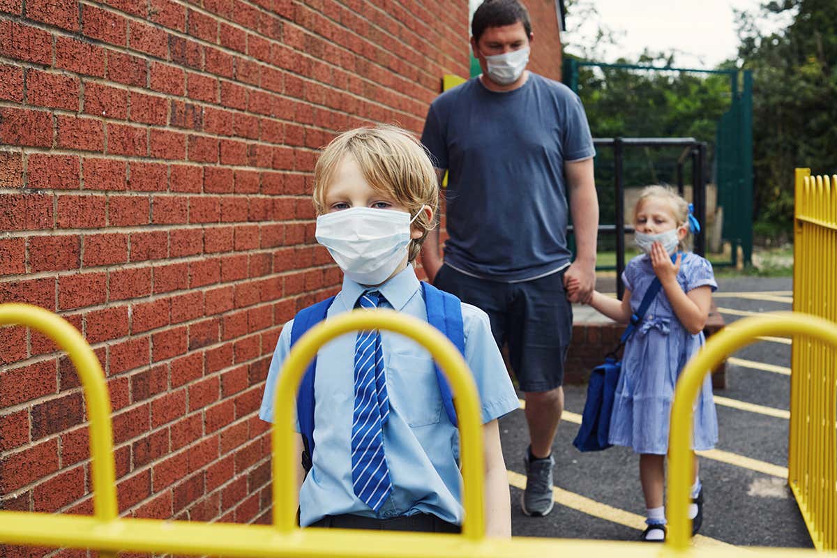 Man and two children wearing face masks walk towards school gate
