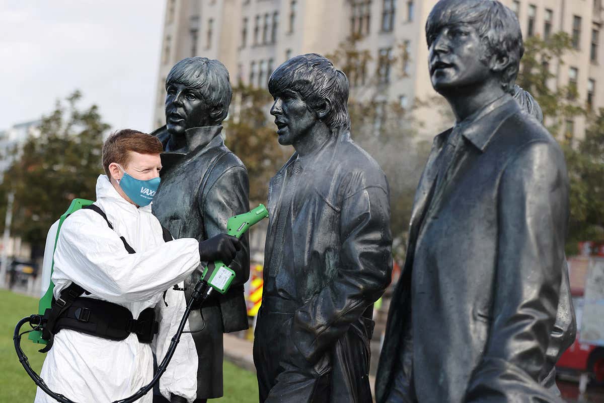 A person wearing protective gear sprays a statue with disinfectant in Liverpool, UK