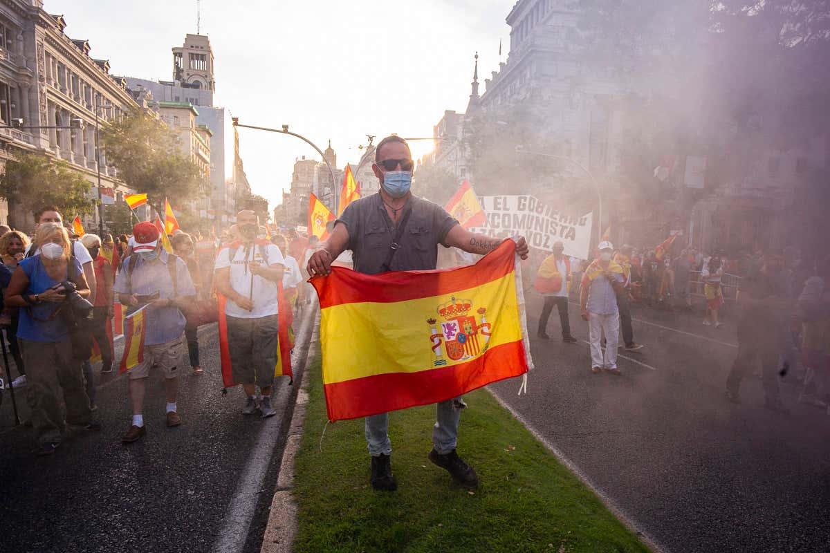 Man wearing face mask carries Spanish flag during protest