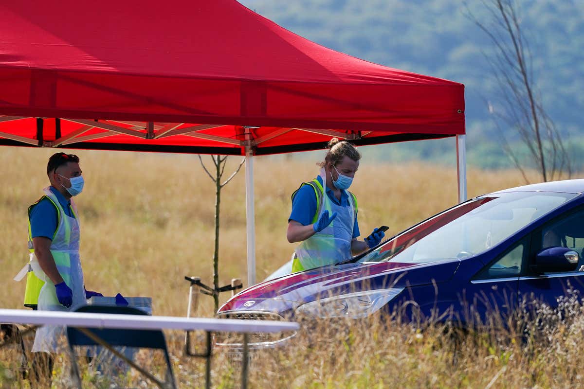 Two people standing outdoors under a gazebo, manning a temporary coronavirus testing facility