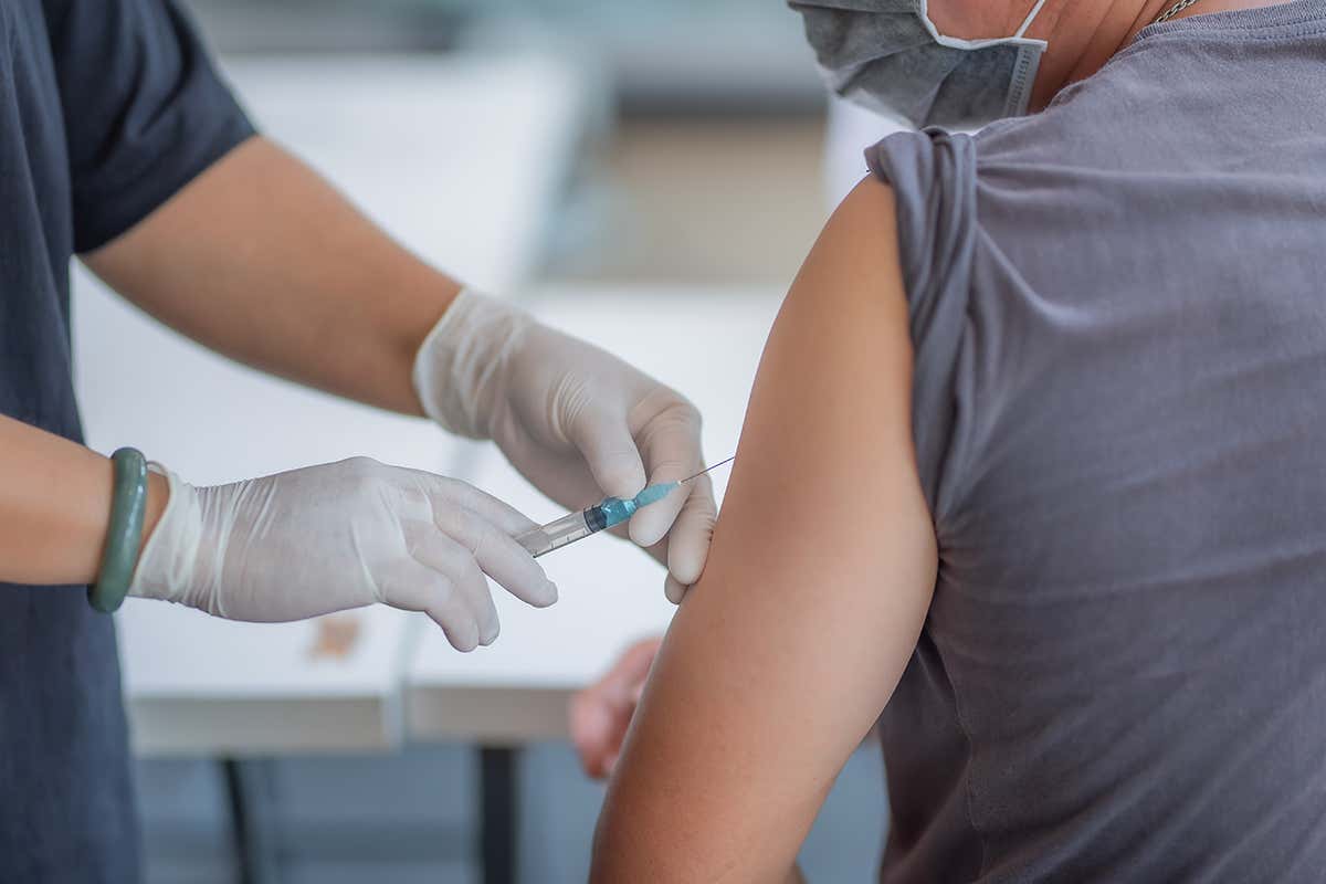 A doctor holds a syringe near a patients arm