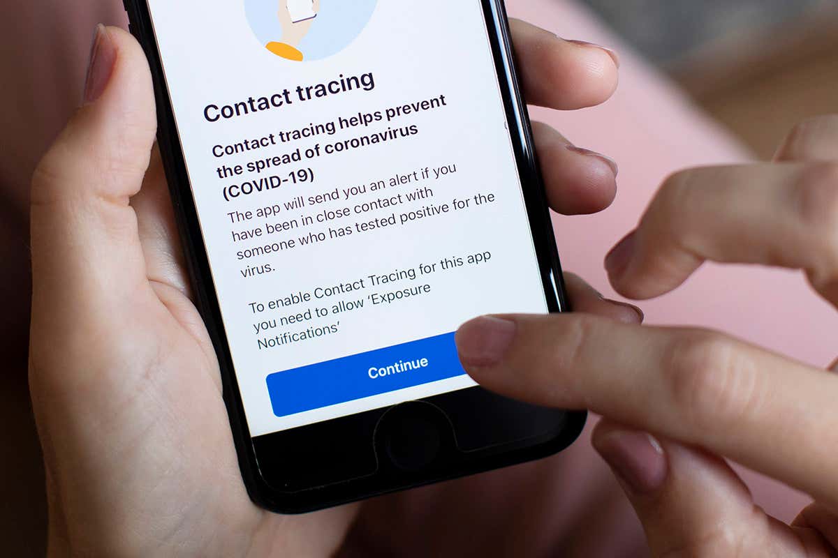 A smartphone being held in a person's hand while they tap on the screen, which is displaying the NHS Covid-19 app