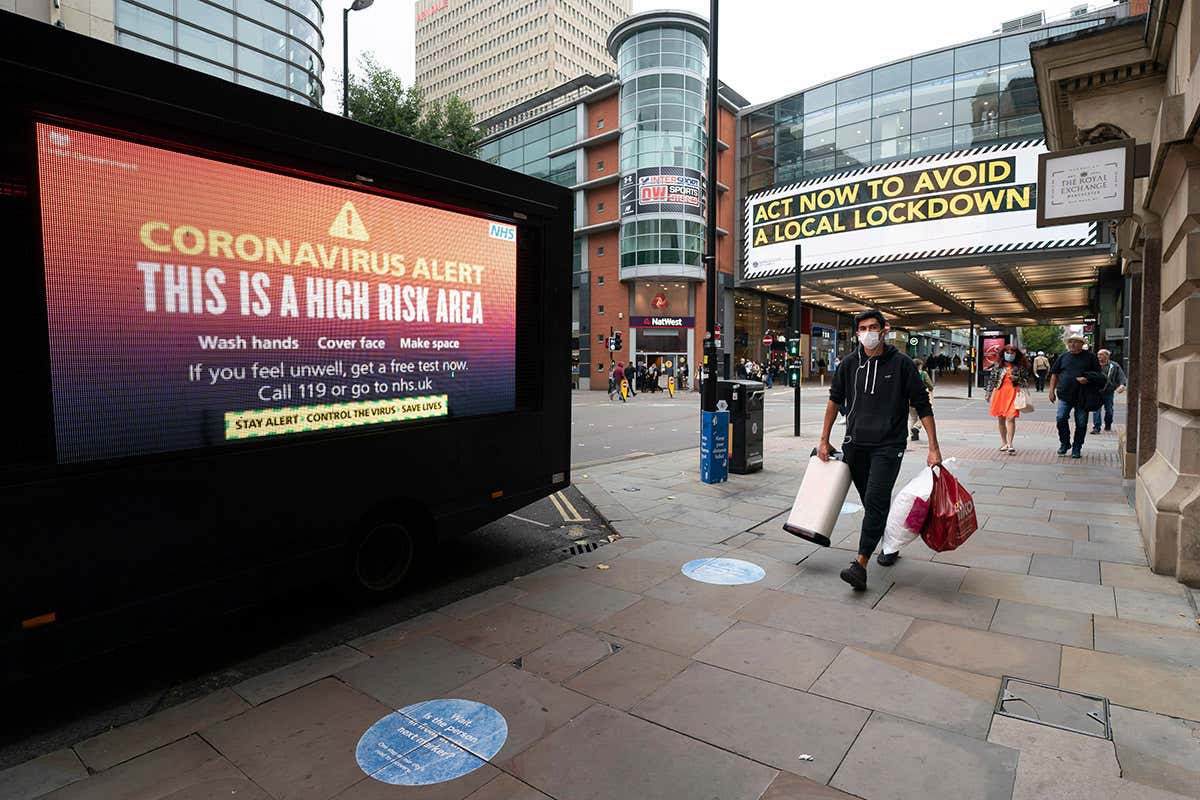 Members of the public are seen by public information messages in central Manchester, England, . The UK has reached "a perilous turning point", Boris Johnson said as he set out a raft of new coronavirus restrictions