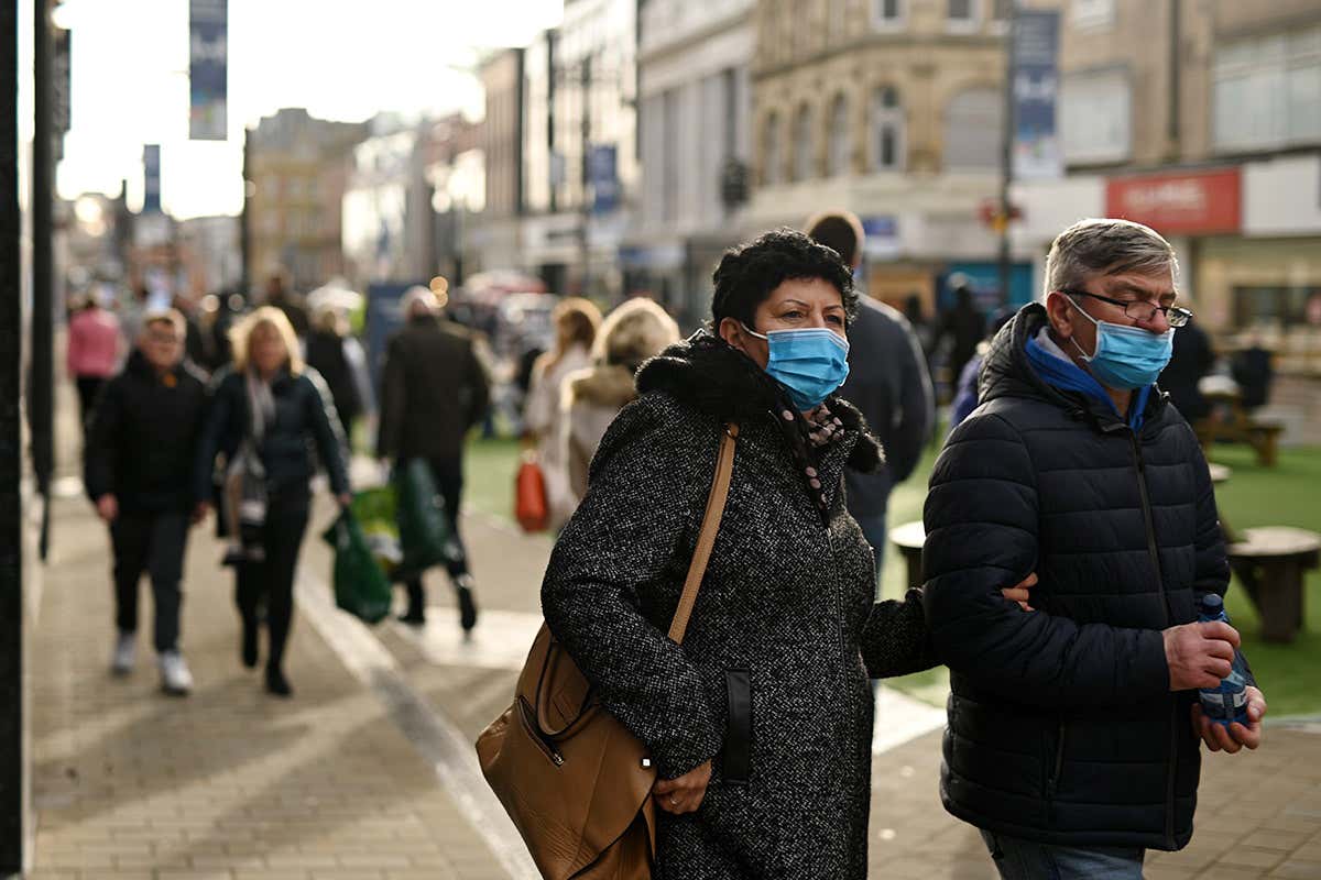 A man and a woman, both wearing face masks, walk with their arms linked in Leeds, UK
