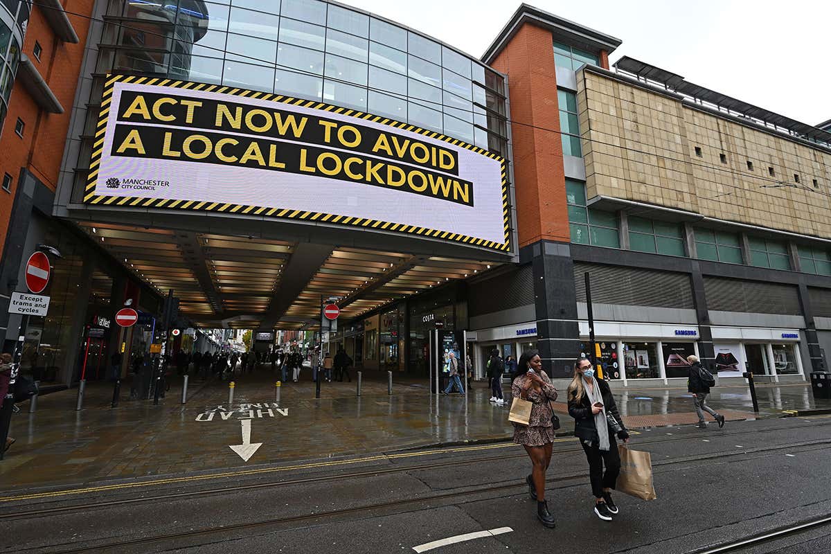 Shoppers wearing face coverings pass beneath an electronic sign reminding pedestrians to "act now to avoid a local lockdown" in Manchester, UK
