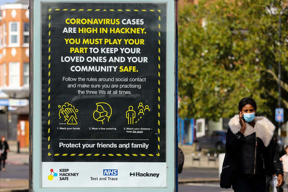 A woman wearing a face covering walks past a public information poster in Hackney, north London