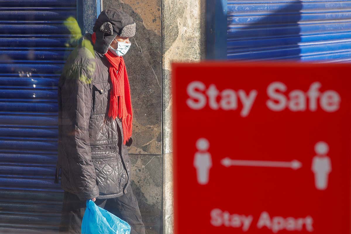 A person wearing a protective mask walks near a social distancing sign in Coventry, UK