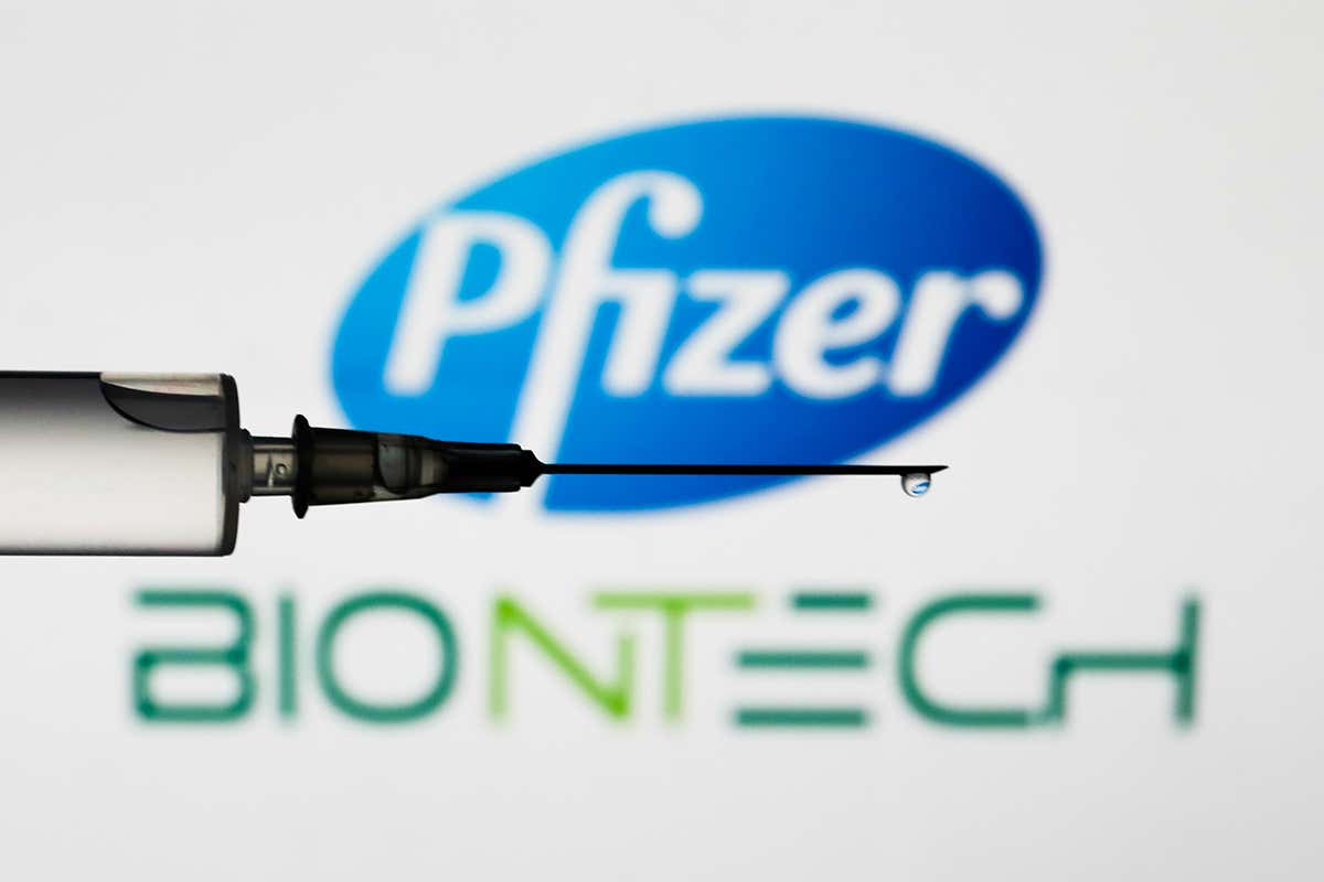 Medical syringe is seen with Pfizer and BioNTech logos displayed on a screen in the background in this illustration photo taken in Poland
