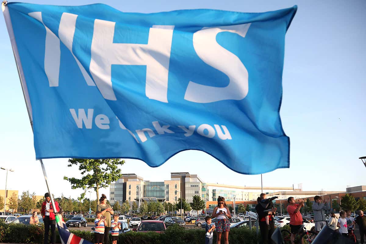 Photo of people standing underneath a blue flag which reads in white letters: NHS We thank you