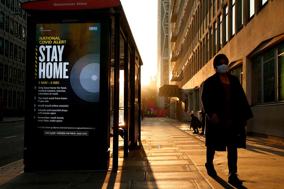 A pedestrian in London wearing a face mask passes a digital display showing the new measures required as England enters a second coronavirus lockdown on 5 November