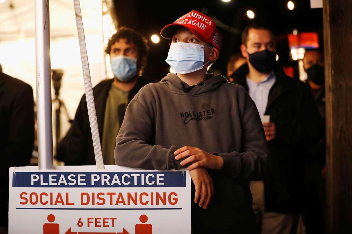 People wearing face masks stand next to a social distancing sign as they watch live election results come in at an election night watch party at Staten Island Republican Party Headquarters in New York City