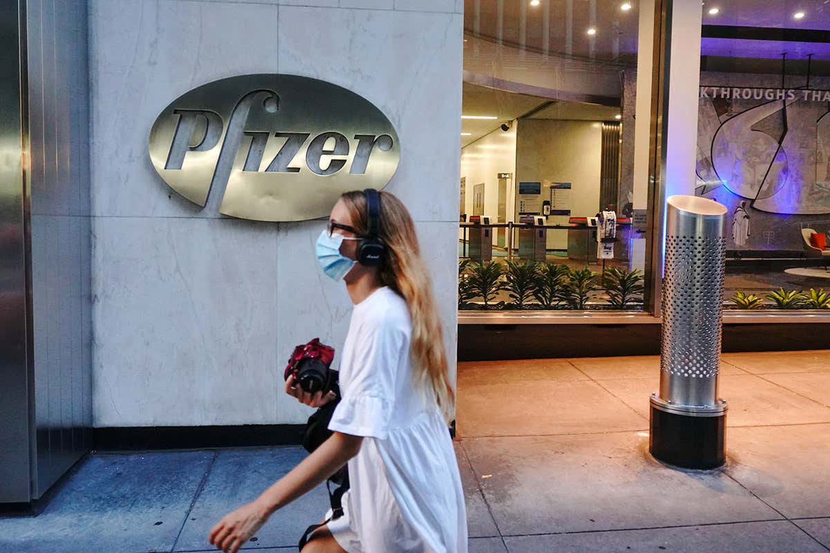 A person wearing a mask walking in front of Pfizer World Headquarters in New York City