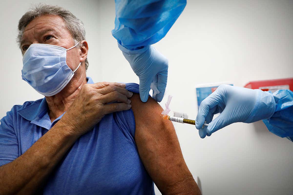 A person wearing a face mask is injected with a needle