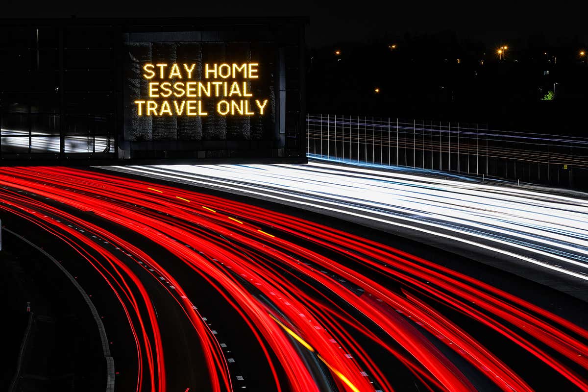Car light trails shine below the stay home, essential travel only sign on the M1 Motorway near Long Eaton in Derbyshire, UK