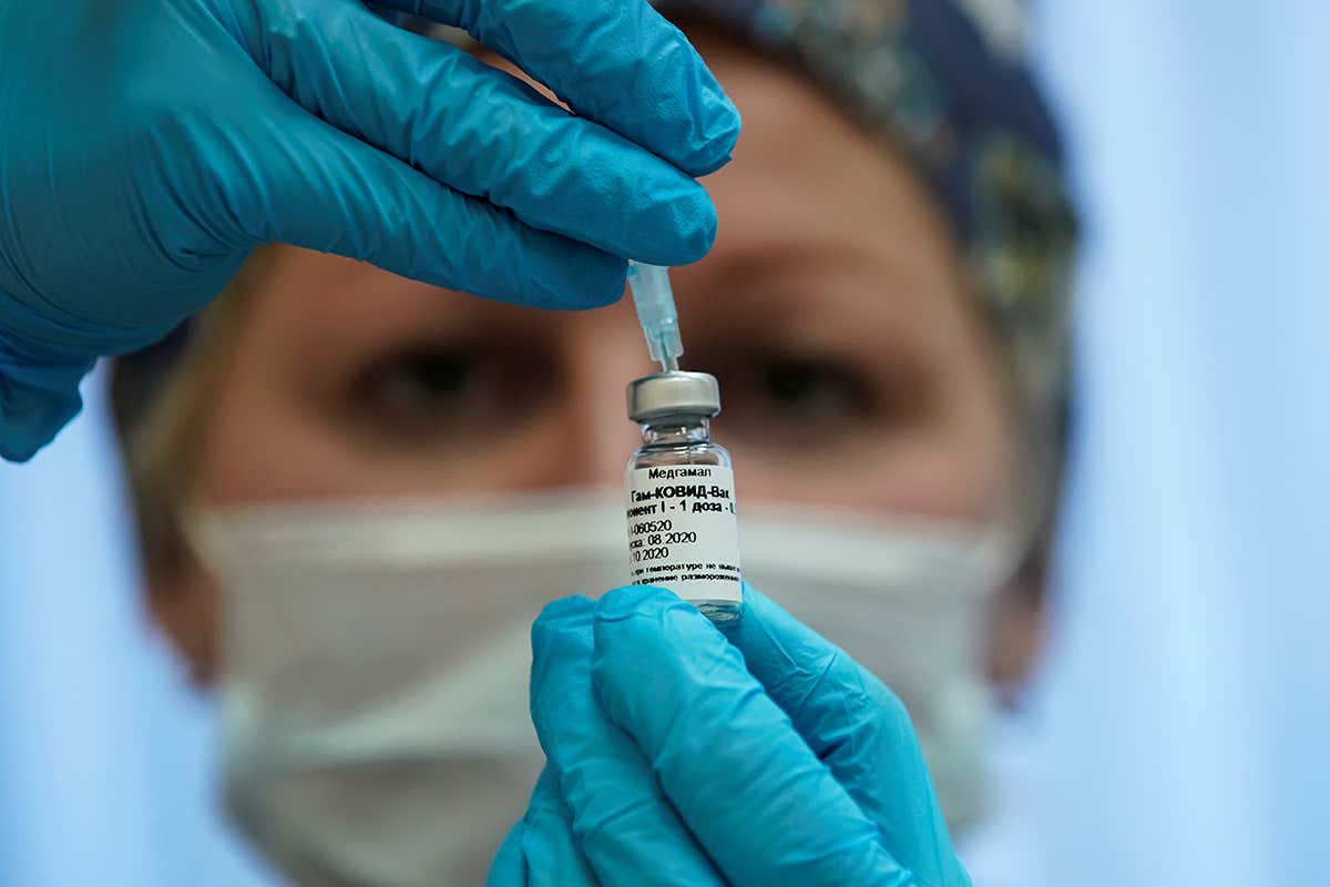 A nurse holds a vaccine vial and syringe in front of her face as she prepares Russia’s Sputnik V coronavirus vaccine for inoculation in a trial in Moscow