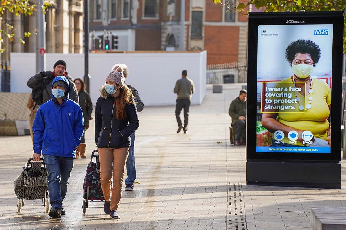People wearing face coverings walk along a shopping street in Hull city centre in England