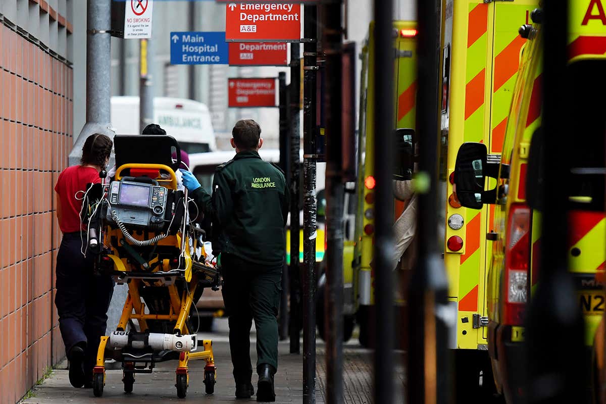 Two paramedics transport a patient on a cart next to an ambulance