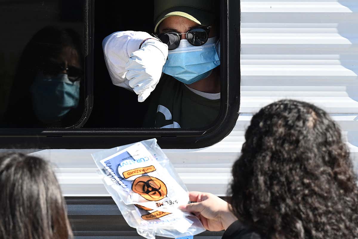 A Community Organized Relief Effort worker hands a coronavirus test kit to two women, at a walk-up covid-19 testing site in Los Angeles, California on 1 December