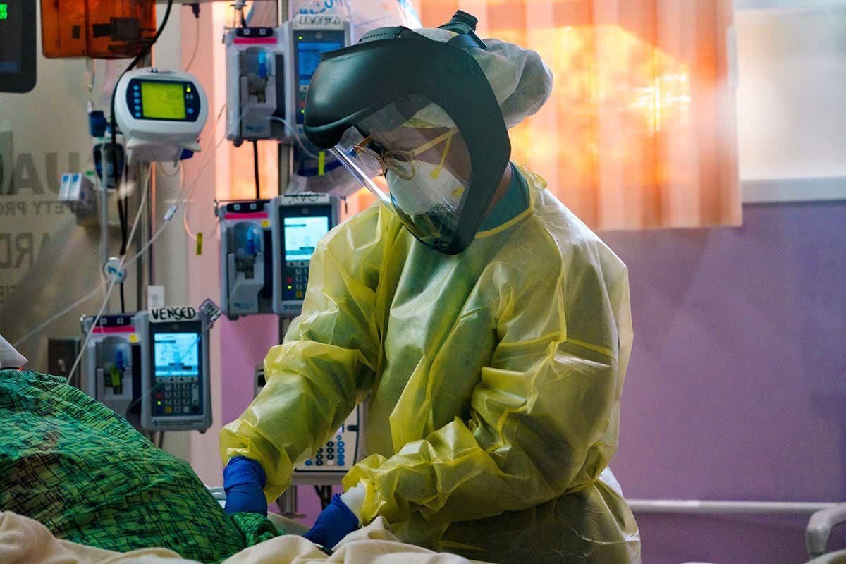 A nurse wearing personal protective equipment, including a face shield, cares for a patient at Scripps Mercy Hospital in Chula Vista, California