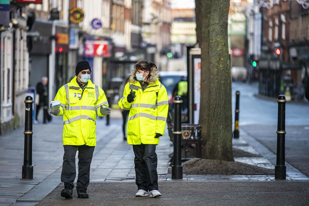 Two covid-19 advisors wearing high-visibility jackets patrol an empty High Street in Worcester city centre, England