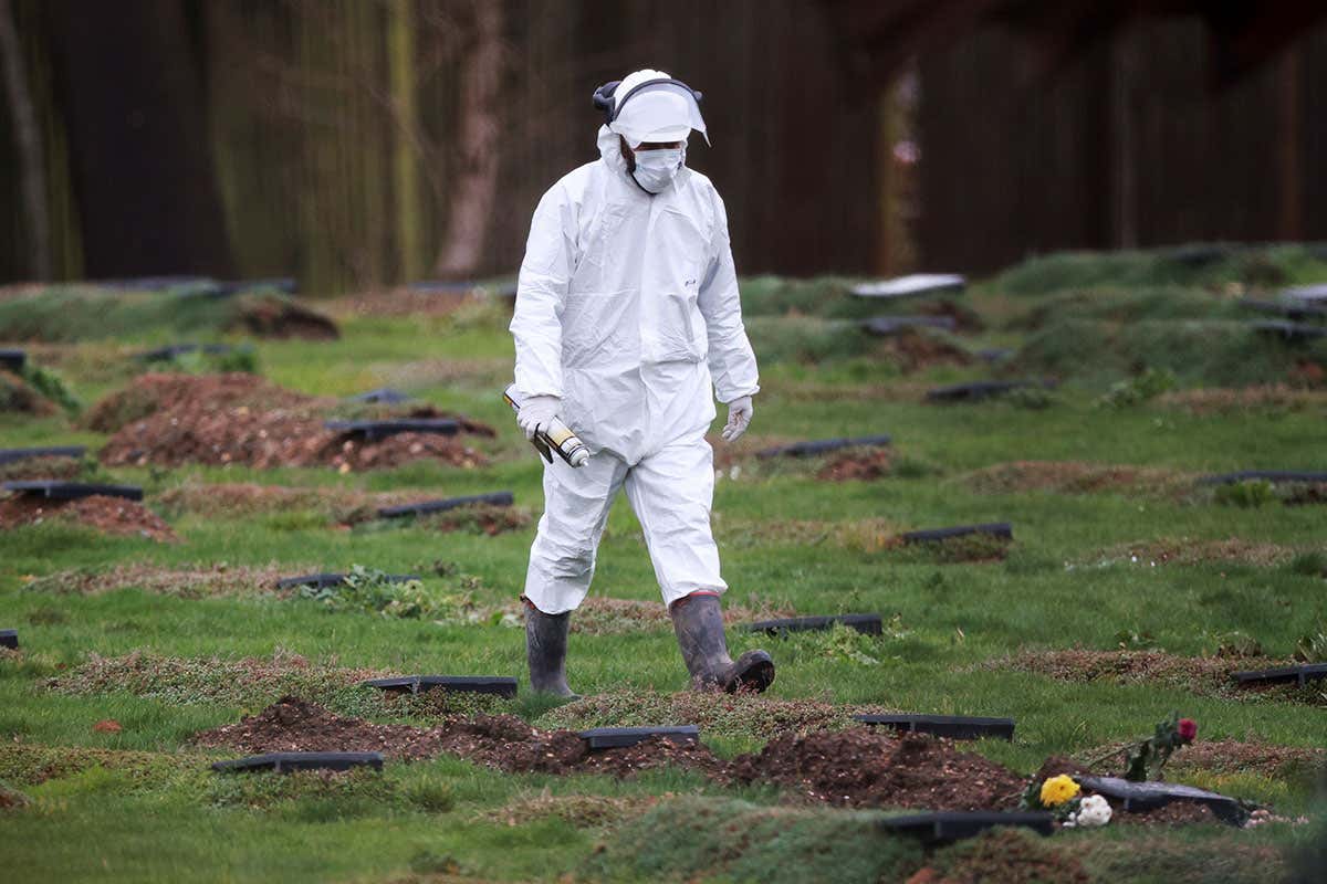 A worker wearing a protective suit walks at a cemetery in Chislehurst, on the outskirts of London, UK