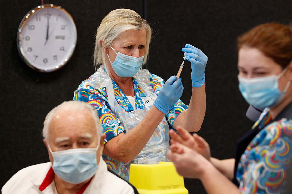A healthcare worker prepares a syringe to inject the Oxford/AstraZeneca covid-19 vaccine, behind a patient waiting in a chair in front