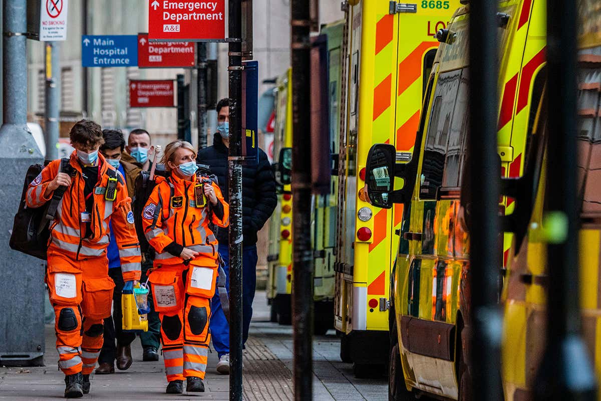 Workers wearing protective clothing walk next to a queue of ambulances outside the Royal London Hospital