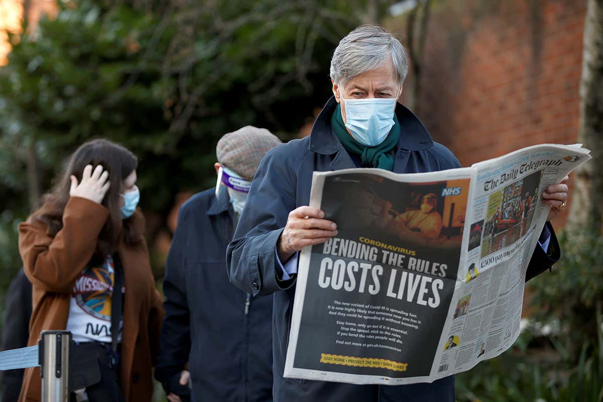 A man reads a newspaper as he waits in a queue