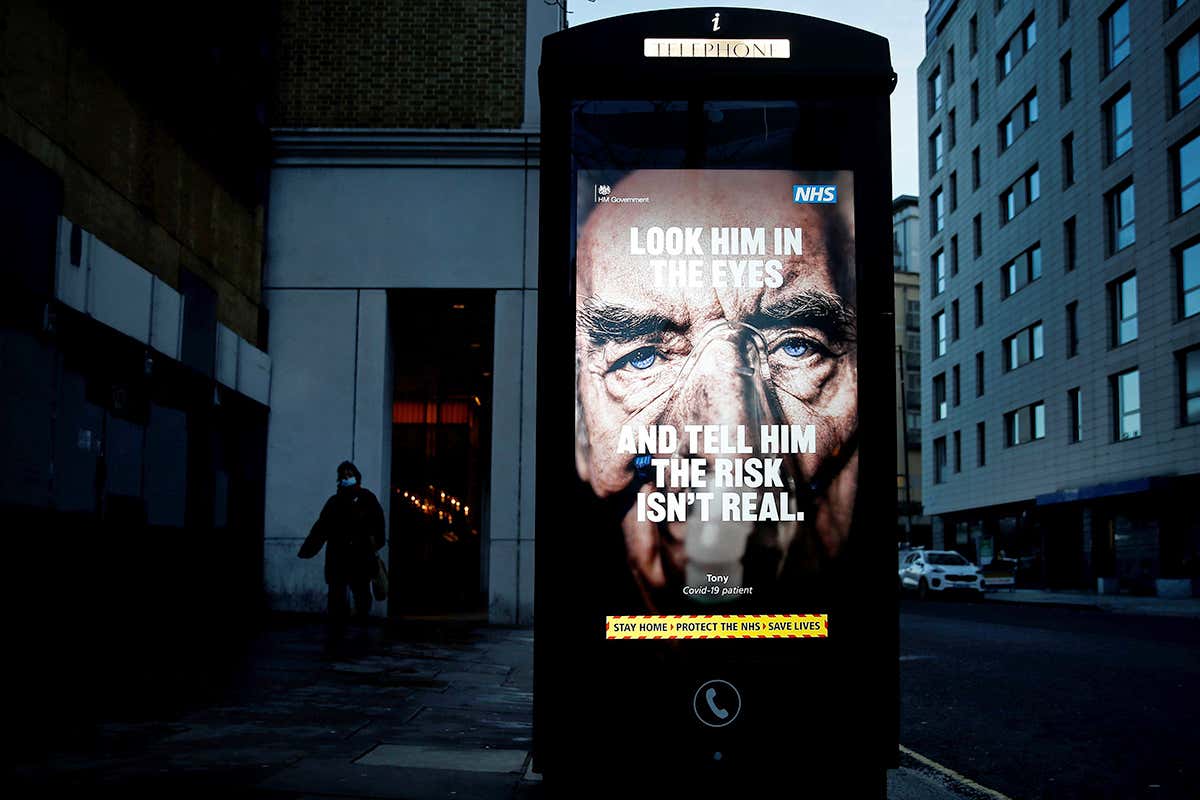 A pedestrian walks past a covid-19 information poster in Victoria train station in central London, which reads: 'look him in the eyes and tell him the risk isn't real' on top of an image of a patient wearing an oxygen mask