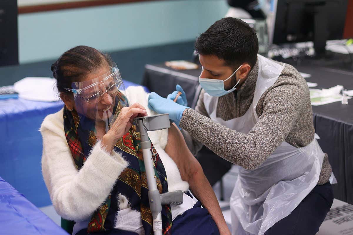 A woman and a healthcare worker wearing personal protective equipment are pictured as the healthcare worker administers a covid-19 vaccine to her