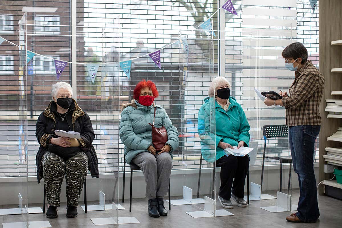 Three people wearing face coverings sit on chairs in a waiting area
