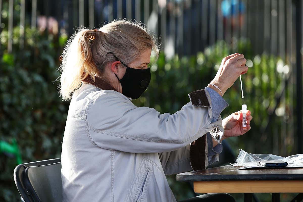 A woman is pictured sitting on a chair, holding a coronavirus test kit