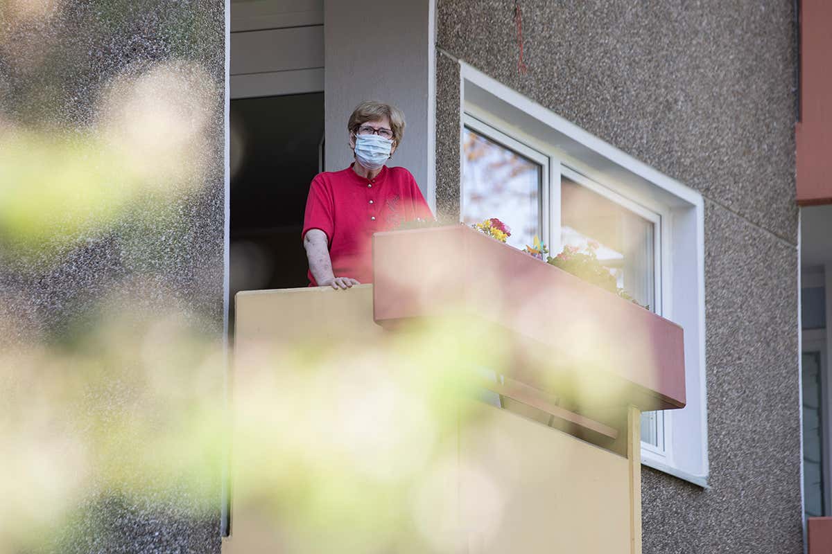 A woman wearing a face mask stands on a balcony in a retirement home