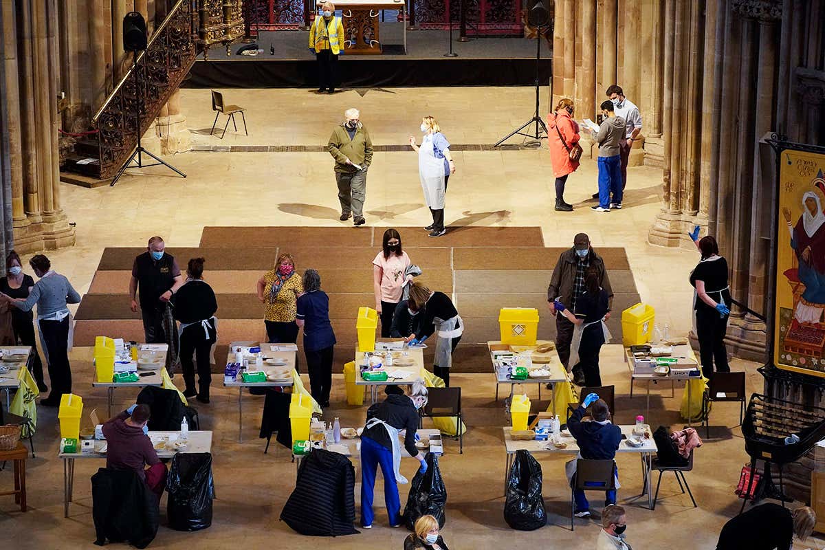 Vaccination centre inside a cathedral is shown with people standing at various covid-19 vaccination stations 