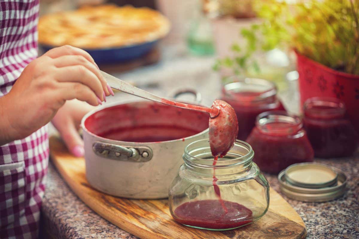 Young women preparing and canning fresh homemade strawberry jam, she pouring him into a jar