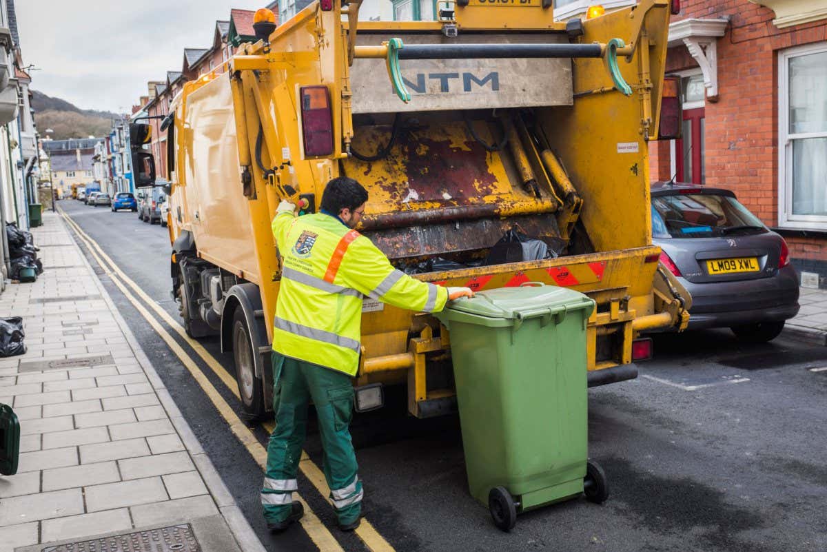 A green rubbish bin being loaded onto a refuse cart in the UK
