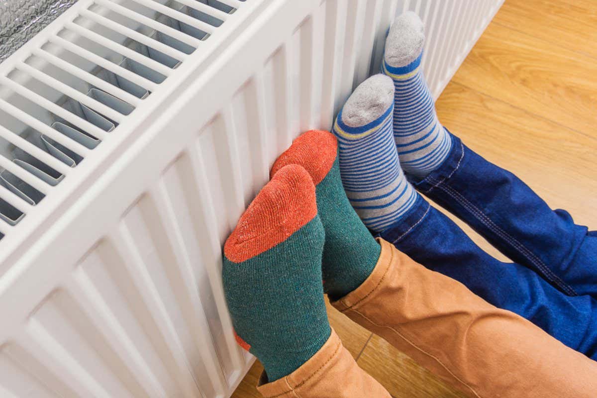 Woman and child wearing colorful pair of woolly socks warming cold feet in front of heating radiator in winter time. Electric or gas heater at home. Part of body, selective focus.