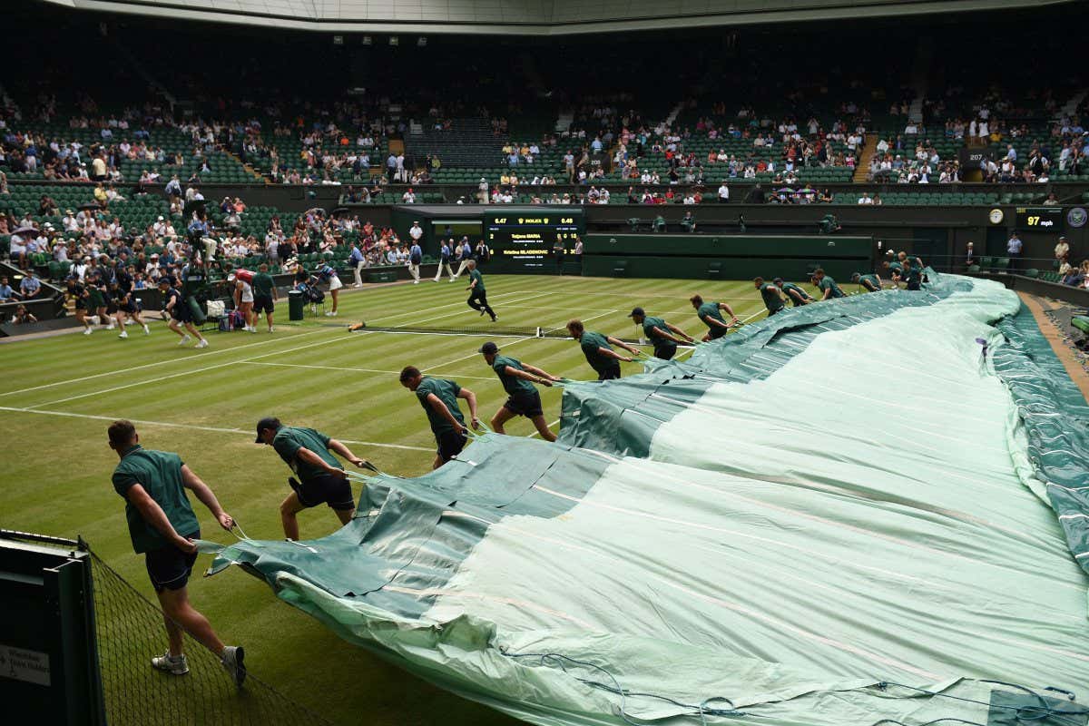 Groundstaff pull the covers over the grass court as rain stops play between Germany's Tatjana Maria and France's Kristina Mladenovic during their women's singles second round match on the third day of the 2018 Wimbledon Championships