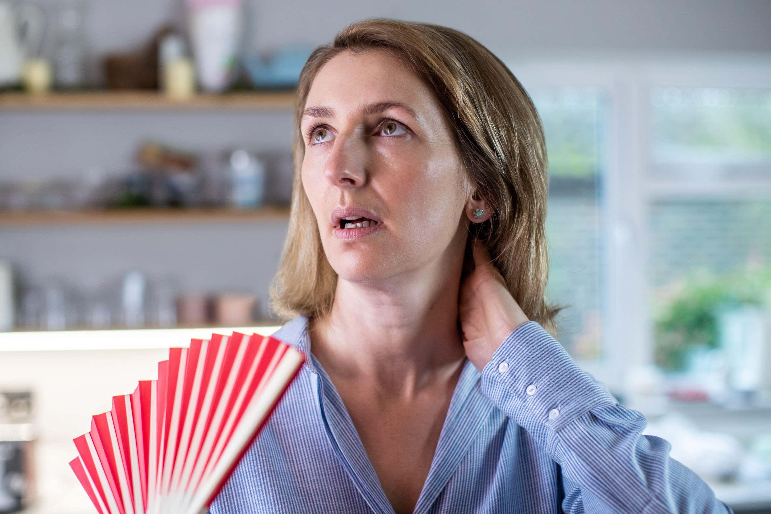 Mature Woman Experiencing Hot Flush From Menopause Using Fan