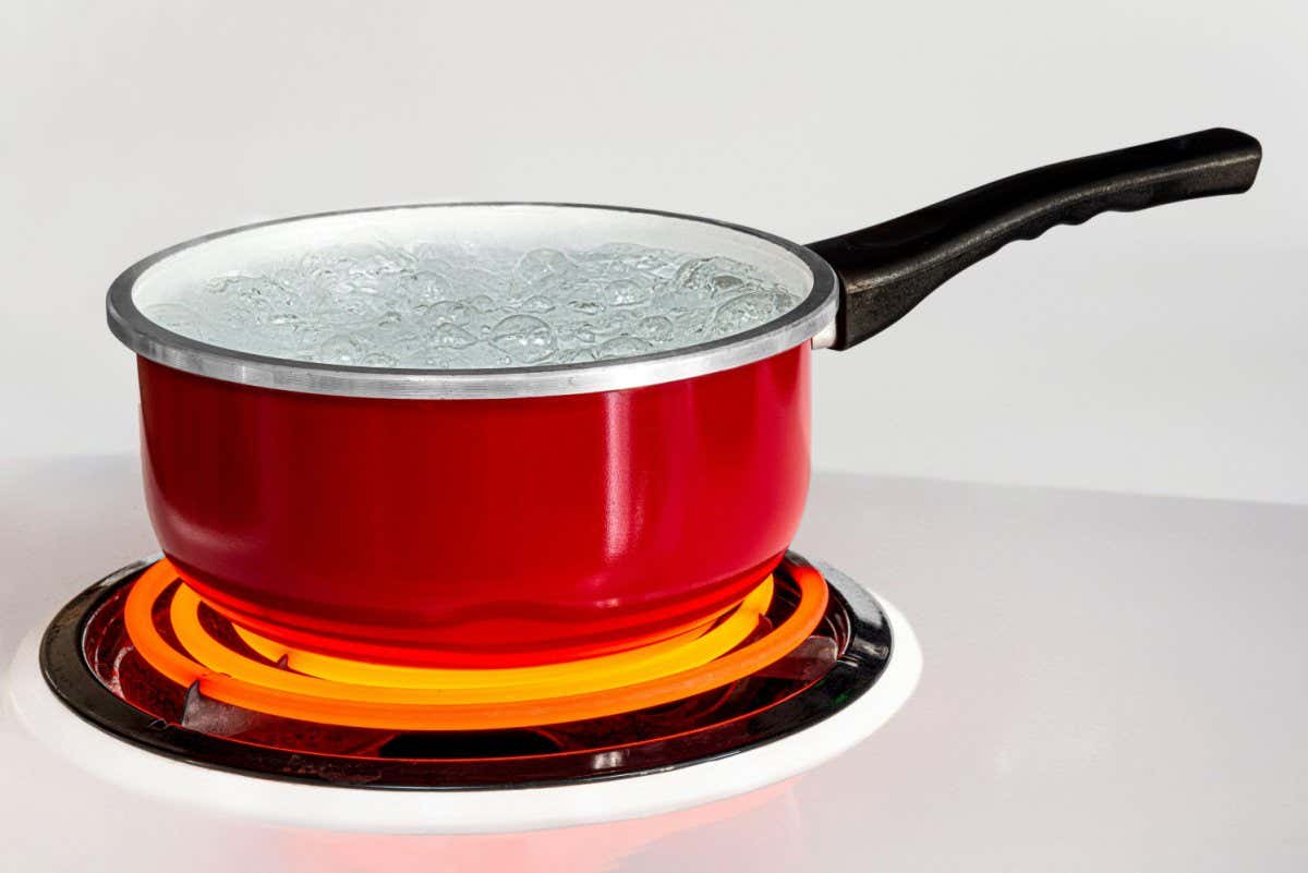 2ARWJ3E Horizontal shot of a red pan of boiling water on top of a stove with the burner turned to high.