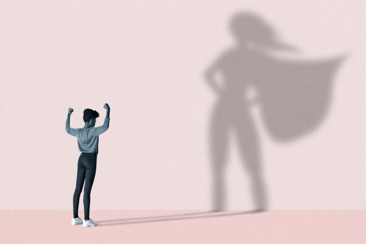 Woman flexing muscles in front of a superhero shadow
