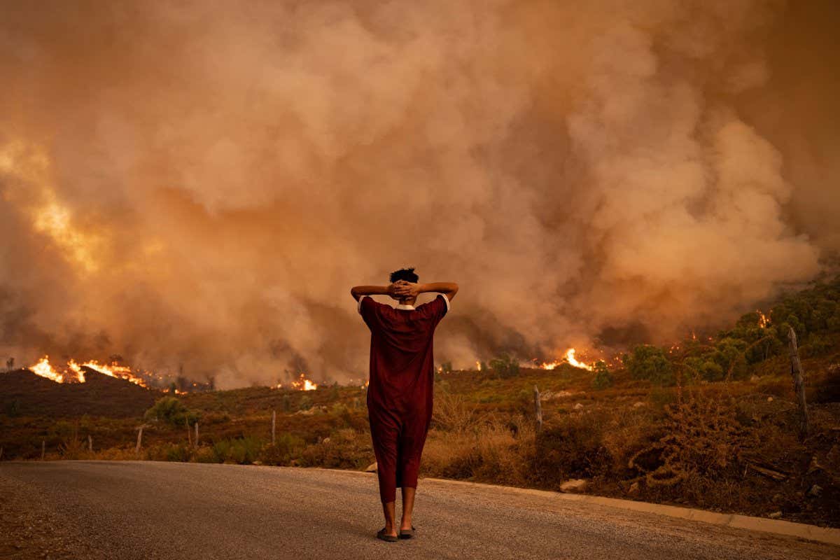 TOPSHOT - A woman looks at wildfires tearing through a forest in the region of Chefchaouen in northern Morocco on August 15, 2021. - Firefighters were battling overnight to put out two forest blazes, a forestries official said as the North African kingdom swelters in a heatwave that saw temperatures of up to 49 degrees Celsius (120 Fahrenheit) on the weekend, according to weather authorities. Morocco joins several other Mediterranean countries that have seen forest fires in recent weeks, including neighbouring Algeria where at least 90 people were killed in wildfires last week. (Photo by FADEL SENNA / AFP) (Photo by FADEL SENNA/AFP via Getty Images)