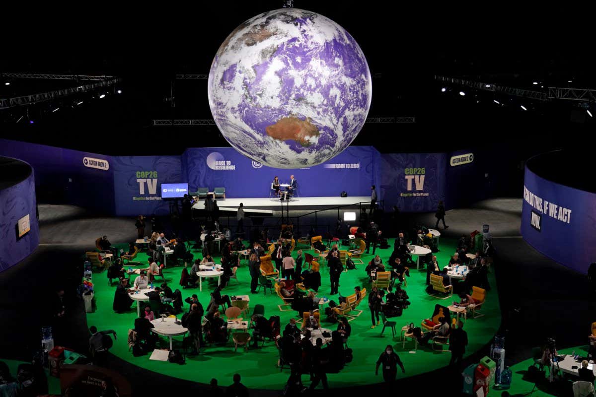 Delegates gather in a large room under a balloon with the Earth printed on it at the COP26 climate summit