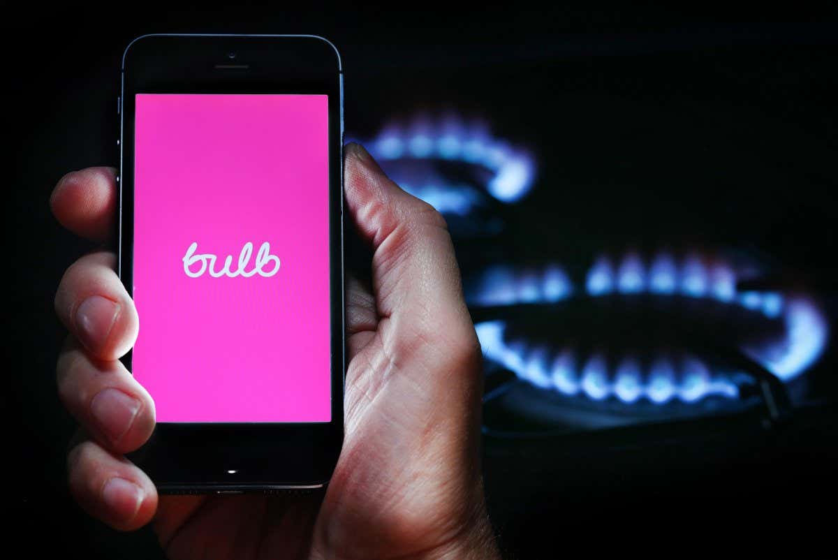 A man looking at the website logo for energy company Bulb on his phone in front of his gas cooker