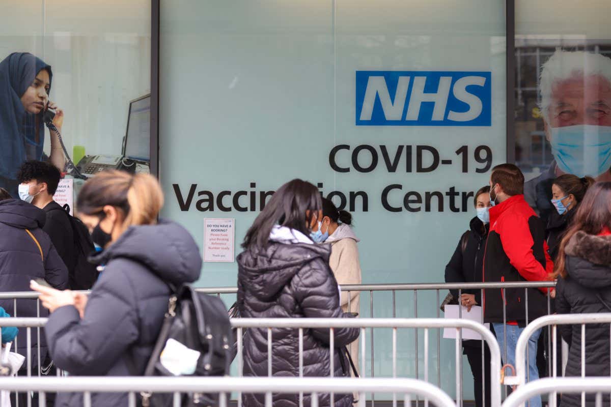Visitors queue for Covid-19 vaccinations at a National Health Service (NHS) walk-in vaccine center at Romford, U.K., on Monday, Dec. 13, 2021. Prime Minister Boris Johnson warned the U.K. is facing a "tidal wave" of omicron infections and set an end-of-year deadline for the countrys booster vaccination program. Photographer: Chris Ratcliffe/Bloomberg via Getty Images
