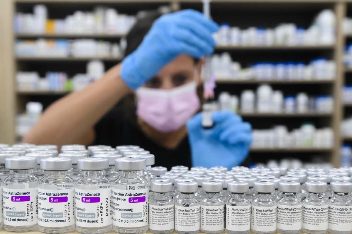 Pharmacist drawing up a dose behind vials of both Pfizer-BioNTech and Oxford-AstraZeneca covid-19 vaccines