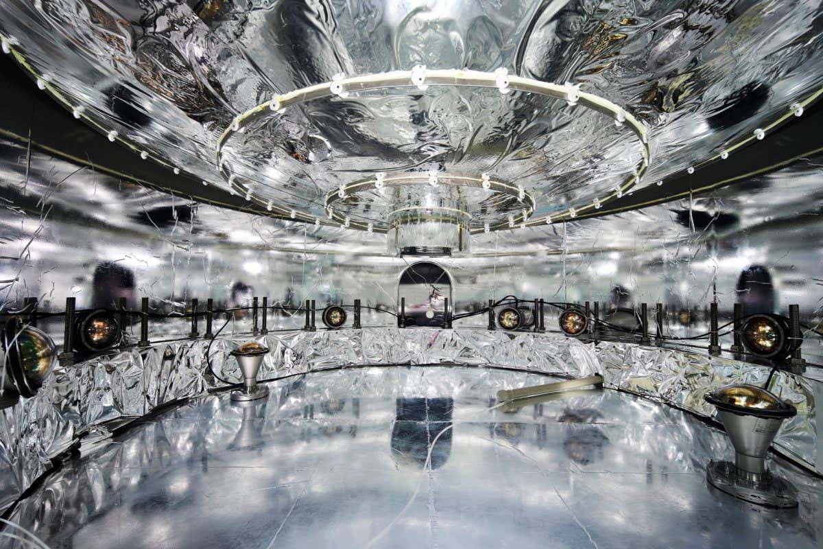 Bottom view of the LEGEND-200 liquid argon cryostat and the enclosing water tank. The inner walls of the water tank and the outer wall of the cryostat are covered with a wavelength-shifting mirror film. The purpose is to shift and reflect the light produced by muons via the Cherenkov effect in the water. The photons are detected by photosensors. The purpose of this detector component is to detect and identify cosmic ray muons, some of which still reach the experiment despite being located deep underground the Gran Sasso mountain. (fyi: The muon flux is reduced by a factor 106 (one million) by the rock). If not identified, the muon induced events could mimic the searched signal events.