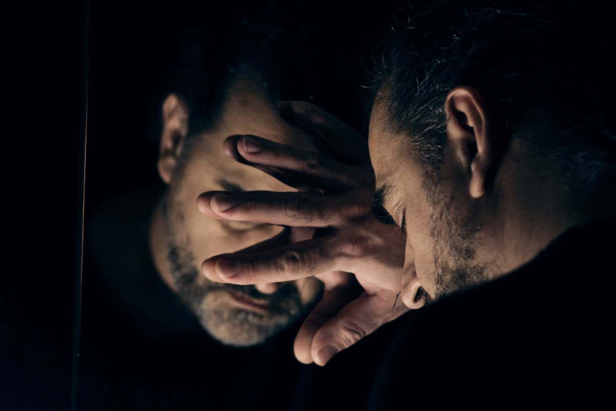 Man in despair, sad and lonely resting his head on a hand, in front of mirror