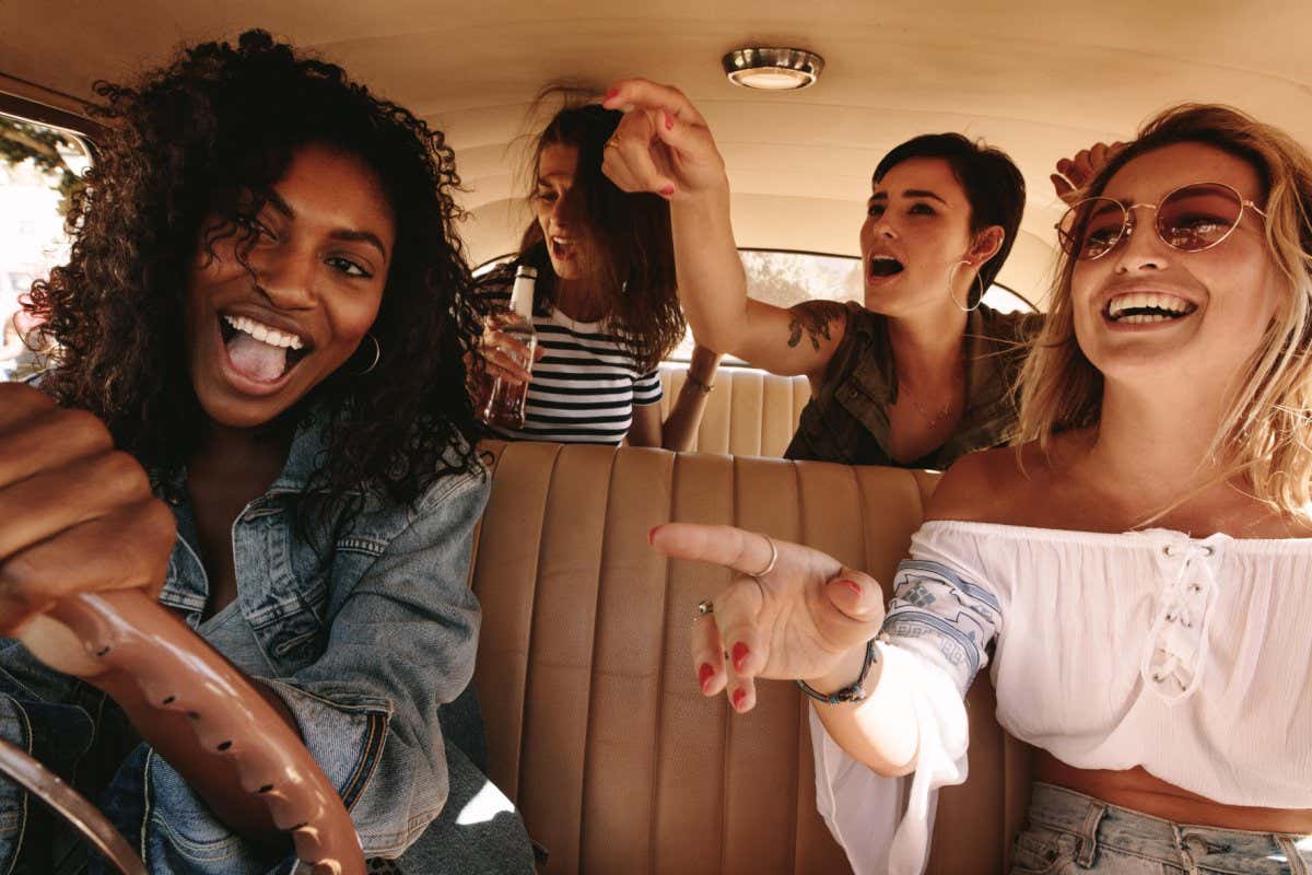 PGDX6B Young african woman driving the car with her friends having fun in the car. Crazy young female friends having lots of fun on road trip.